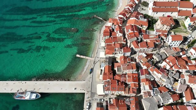 Baska beach and coastline with crystal-clear turquoise water, marina boats, city street, sunny summer mood captured from drone view on Krk Island. Baska vacations town in Adriatic sea