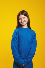 Fototapeta premium Joyful youngster wearing a cozy blue sweater, standing confidently with a cheerful smile on a vivid yellow background. Perfect for children fashion ads and cheerful marketing materials.