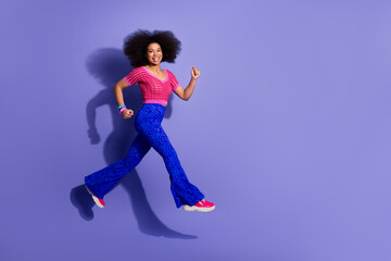 Excited young woman posing energetically in retro inspired fashion against a vibrant purple backdrop, highlighting trendy style