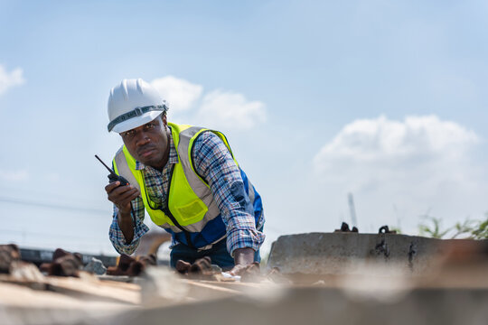 Railroad Maintenance Worker Inspecting Tracks with Communication Device, Engineer Man in Hard Hat and Safety Vest on Outdoor Project, African American Construction Worker with Walkie-Talkie on Site