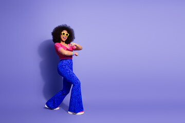 Stylish young woman in retro outfit dancing cheerfully against a vibrant purple background