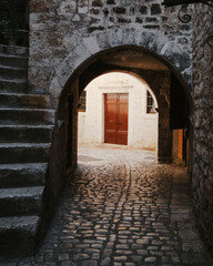 Dark archway the old town. Narrow alley leading to the arch inside stone wall. Light coming through the arch, beige wall with wooden door in the background.