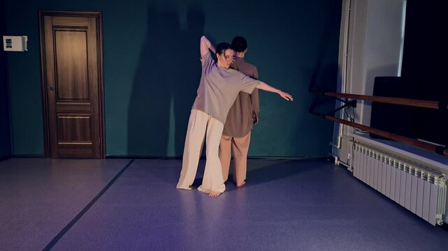 One woman is holding hand on her partner back and dancing together in modern style filmed in the class. Rehearsal of ballet female duet performing contemporary choreography. Sensuality and music
