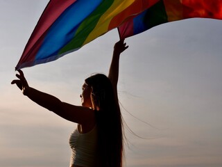 Rainbow flag of an LGBT organization waving against a blue sky. LGBT pride flags include lesbians,...
