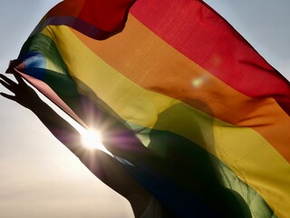 Rainbow flag of an LGBT organization waving against a blue sky. LGBT pride flags include lesbians,...