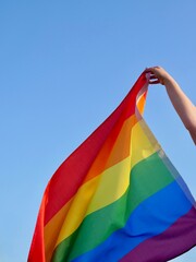 Rainbow flag of an LGBT organization waving against a blue sky. LGBT pride flags include lesbians, gays, bisexuals and transgender diversity people.
