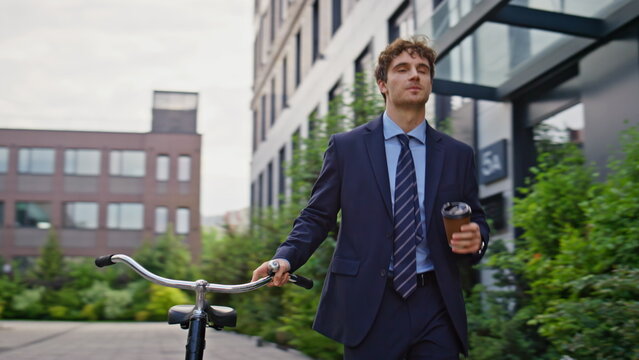 Confident businessman walking bicycle enjoying coffee outdoors. Man smiling - Powered by Adobe