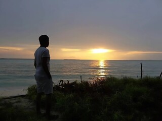 Fototapeta premium silhouette of a man standing on the beach at sunset