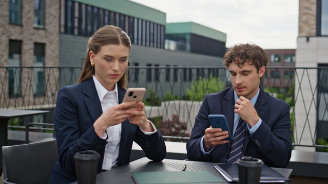 Business colleagues focusing smartphones outdoors at work break closeup. 