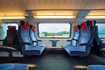 Blue empty opposing, first class seats in a moving train. Large window, daytime, summer, no people.