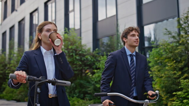 Corporate colleagues walking downtown closeup. Businesswoman riding scooter