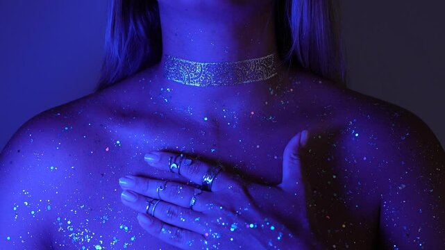 A young mesmerising cosmic woman breathes deeply with her hand on her heart. Light glows from her chest, symbolizing inner awakening. The glittering skin reveals the silent power of remembrance