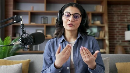Webcam view. Young woman recording podcast looking at camera using microphone in home office. Female vlogger influencer conducts online broadcast, interview or webinar, speaks remotely via video call