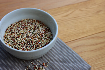 Close-up of mix of raw black, red and white quinoa seeds in a ceramic bowl on wooden table