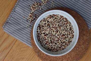 Top view of mix of raw black, red and white quinoa seeds in a ceramic bowl on wooden table