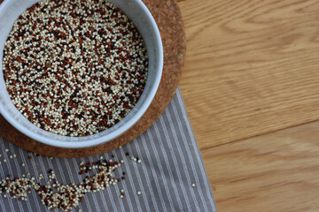 Top view of mix of raw black, red and white quinoa seeds in a ceramic bowl on wooden table