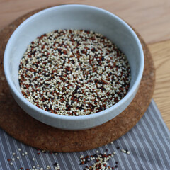 Close-up of mix of raw black, red and white quinoa seeds in a ceramic bowl on wooden table