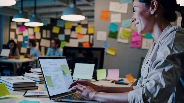 Woman Focused Work: A focused woman works diligently at her desk, engrossed in her work with a laptop, amidst a creative and collaborative office atmosphere.