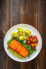 Seared salmon steak with cherry tomato salad and boiled potatoes on wooden table	