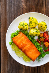 Seared salmon steak with cherry tomato salad and boiled potatoes on wooden table	