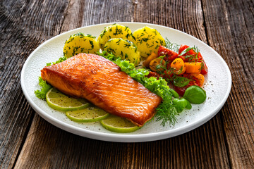 Seared salmon steak with cherry tomato salad and boiled potatoes on wooden table	