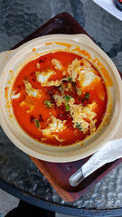 Spicy Asian soup served in a clay pot, filled with fresh red broth, soft tofu, vegetables, and chili oil. Culinary concept, restaurant, or traditional food.