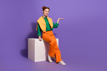 Young stylish woman in vibrant outfit gesturing enthusiastically against a purple backdrop,...