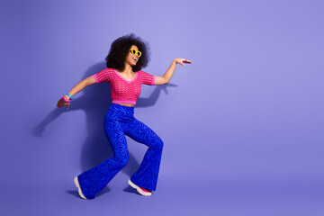 Confident young woman in vibrant retro attire posing dynamically on a purple background, expressing...