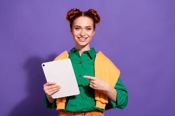 Obraz premium Lovely young woman with red hair holding a tablet and pointing at it against a vibrant purple background