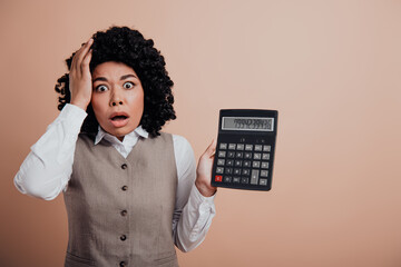 Young businesswoman in formal attire expressing surprise while holding a large calculator against a...
