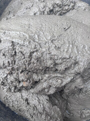 Image shows a close-up view of wet cement or concrete. The surface appears rough and textured, with some areas showing small pebbles or aggregate particles embedded within the mixture.