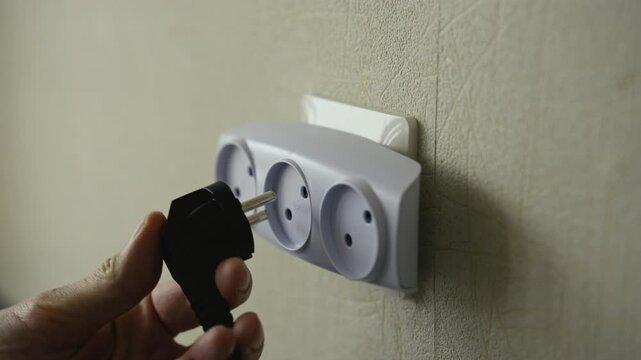 Male hand connecting black electrical plug to white triple wall socket, demonstrating precise wiring connection and professional electrical installation technique, close-up. Shooting in slow motion.