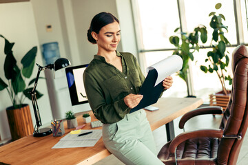 Elegant businesswoman analyzing documents in a modern office setting with natural light and stylish...