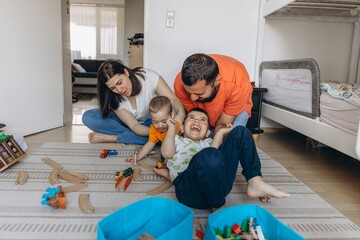 Parents playing and laughing with their two sons in a bright children room. Family bonding, playful...