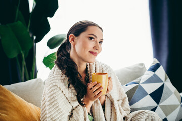 Young woman enjoying a cozy morning with warm beverage indoors, wrapped in blanket, radiating...