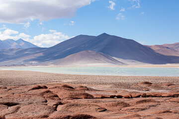 Expansive view of the Atacama Desert's unique landscape, featuring a stunning salt lake and imposing mountains under a blue sky. Ideal for ecotourism and travel