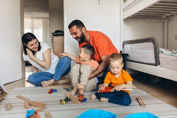 Parents playing and laughing with their two sons in a bright children room. Family bonding, playful...
