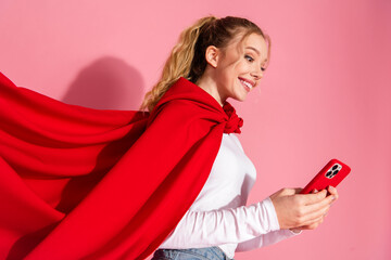 Naklejka premium Cheerful young woman in casual attire holding a smartphone while posing against a vibrant pink background with a confident smile