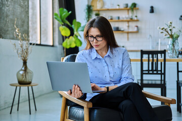 Middle aged business woman sitting in chair typing on laptop computer