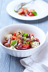 Simple salad with cherry tomatoes, red onion and fresh herbs. Bright wooden background. Close up.	