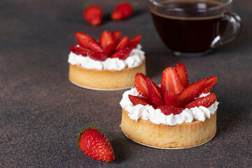 Tarts with fresh strawberries and cup of coffee on brown background