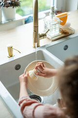 Closeup of children's hands washing a plate near the sink in the kitchen. Eco dishwashing brush.