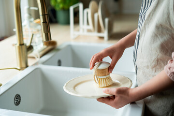 Closeup of children's hands washing a plate near the sink in the kitchen. Eco dishwashing brush.