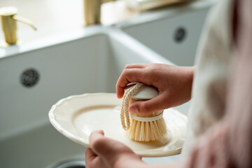 Closeup of children's hands washing a plate near the sink in the kitchen. Eco dishwashing brush.