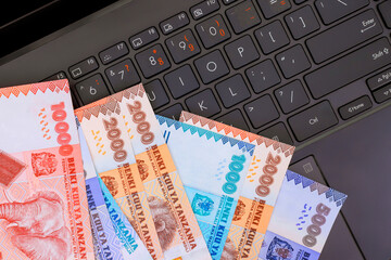 Tanzanian shilling cash banknotes on laptop keyboard, representing online finance digital transactions in an office.
