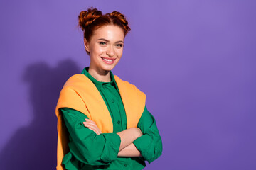 Casual young woman with red hair in green shirt and orange cardigan posing against vibrant purple...
