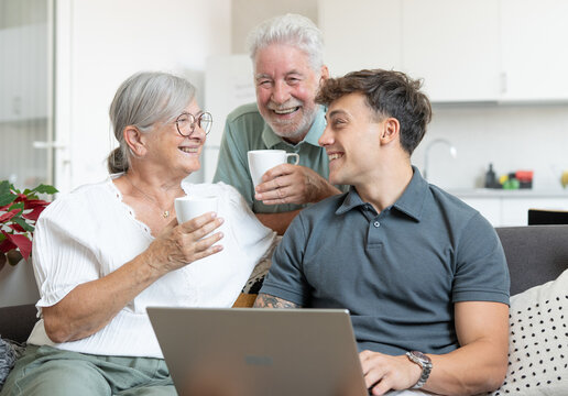 Happy multigenerational family sitting on sofa using laptop together - grandparents with young grandson enjoying carefree moments together learning use of computer