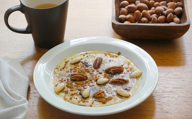 Healthy gluten free porridge cooked from buckwheat and corn semolina and served on white plate with cinnamon, maple syrup, butter and nuts. Morning porridge with mug of tee and nuts on wooden table.