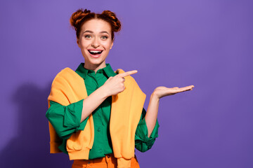 Happy young woman in green shirt and orange sweater posing against purple background with a...