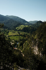 Fototapeta premium Panoramic spring view of Tara National Park with canyon, river, forest and distant village rooftops. Travel in Serbia country concept.